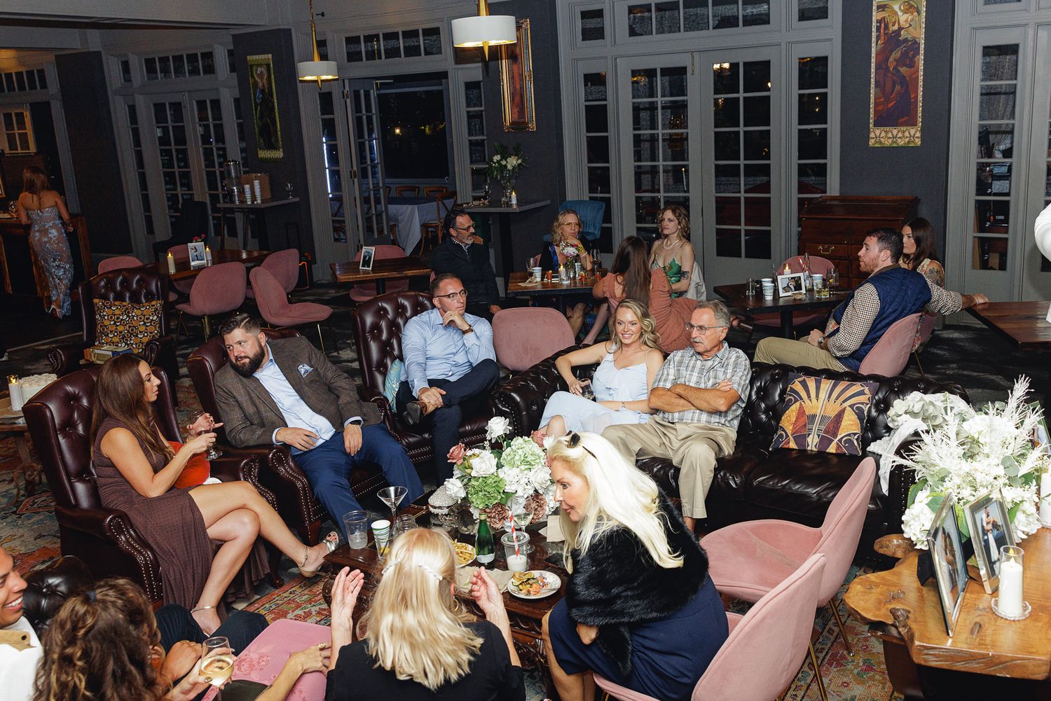Guests socializing at an elegant indoor gathering, seated on plush chairs in a dimly lit upscale venue.
