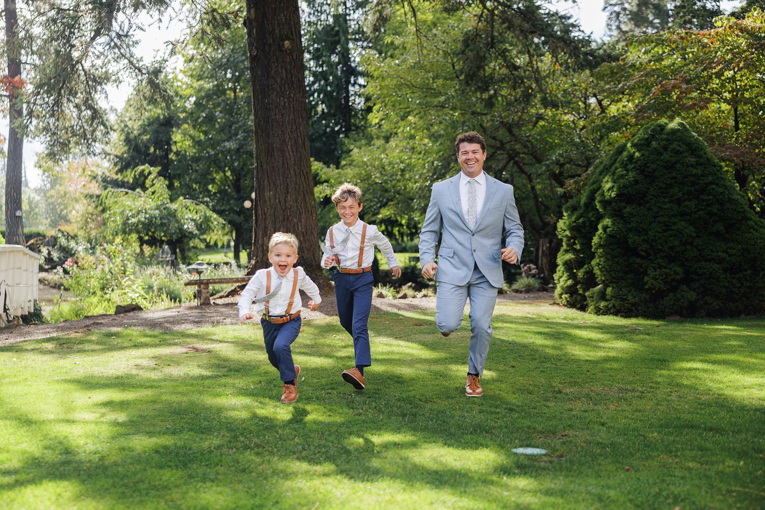 A family runs and plays together on a grassy slope in a sunny park setting.