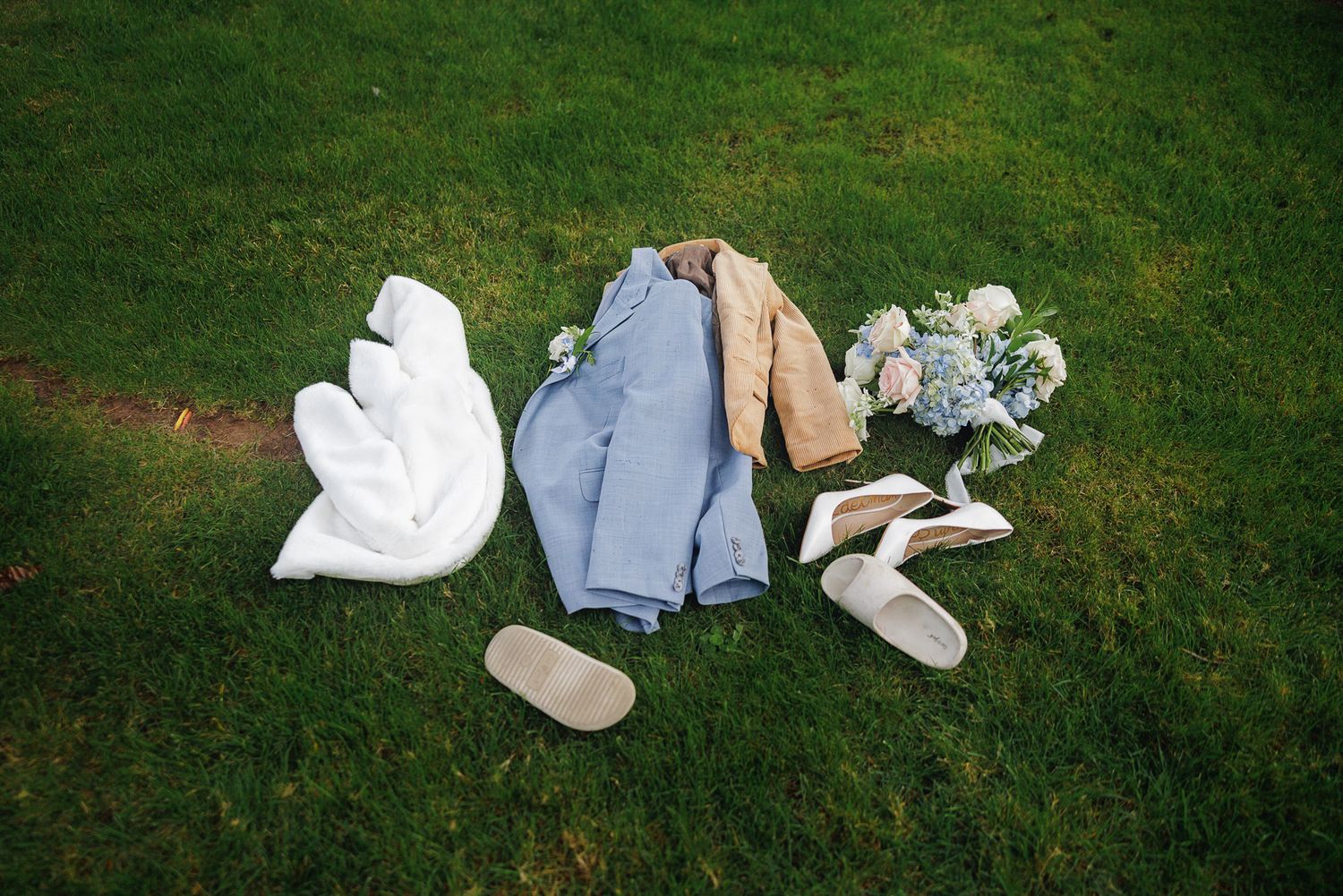 White wedding shoes arranged in a line on lush green grass, creating a romantic outdoor setting.