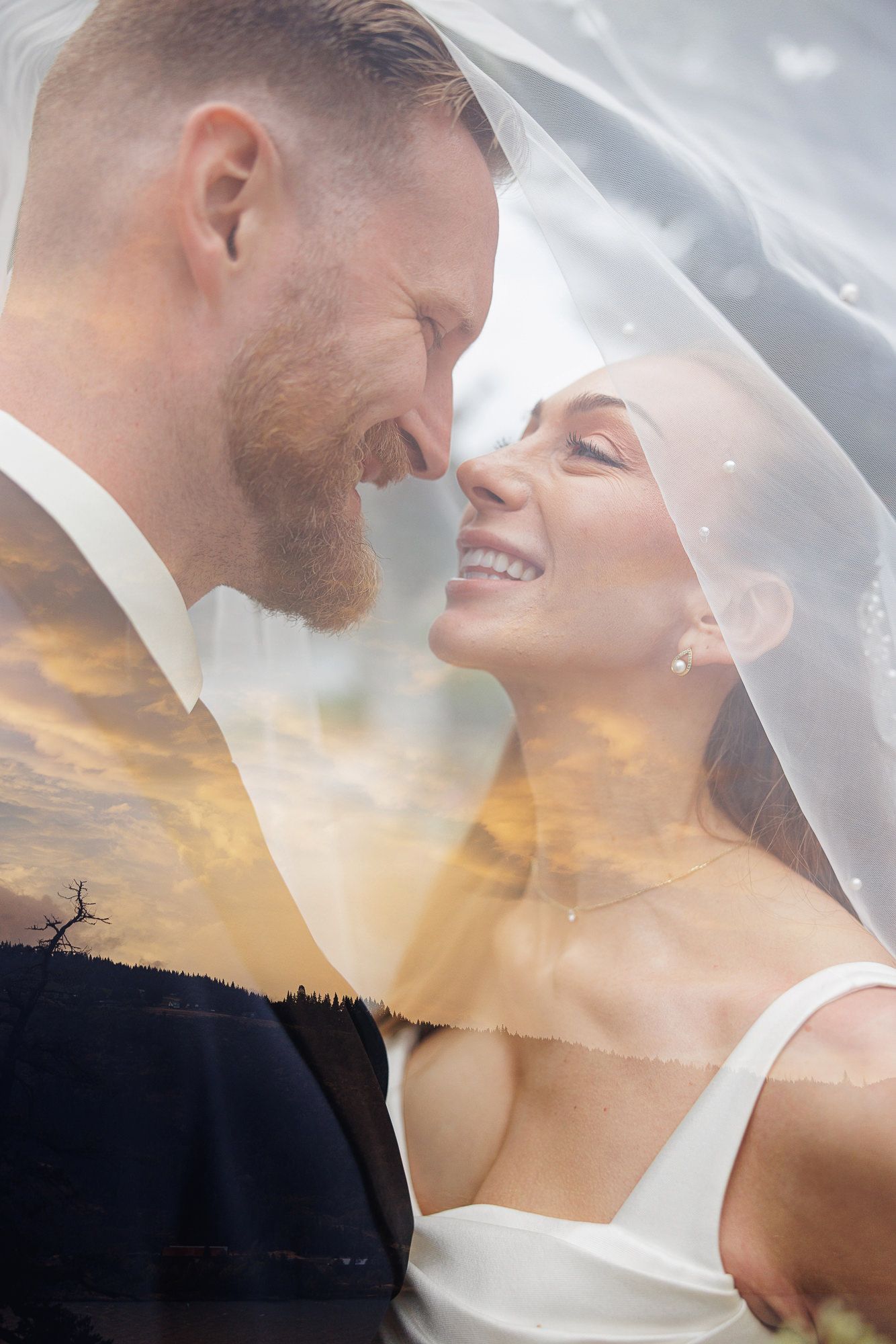 A joyful bride and groom share an intimate moment under a wedding veil with a dreamy double exposure sunset backdrop.