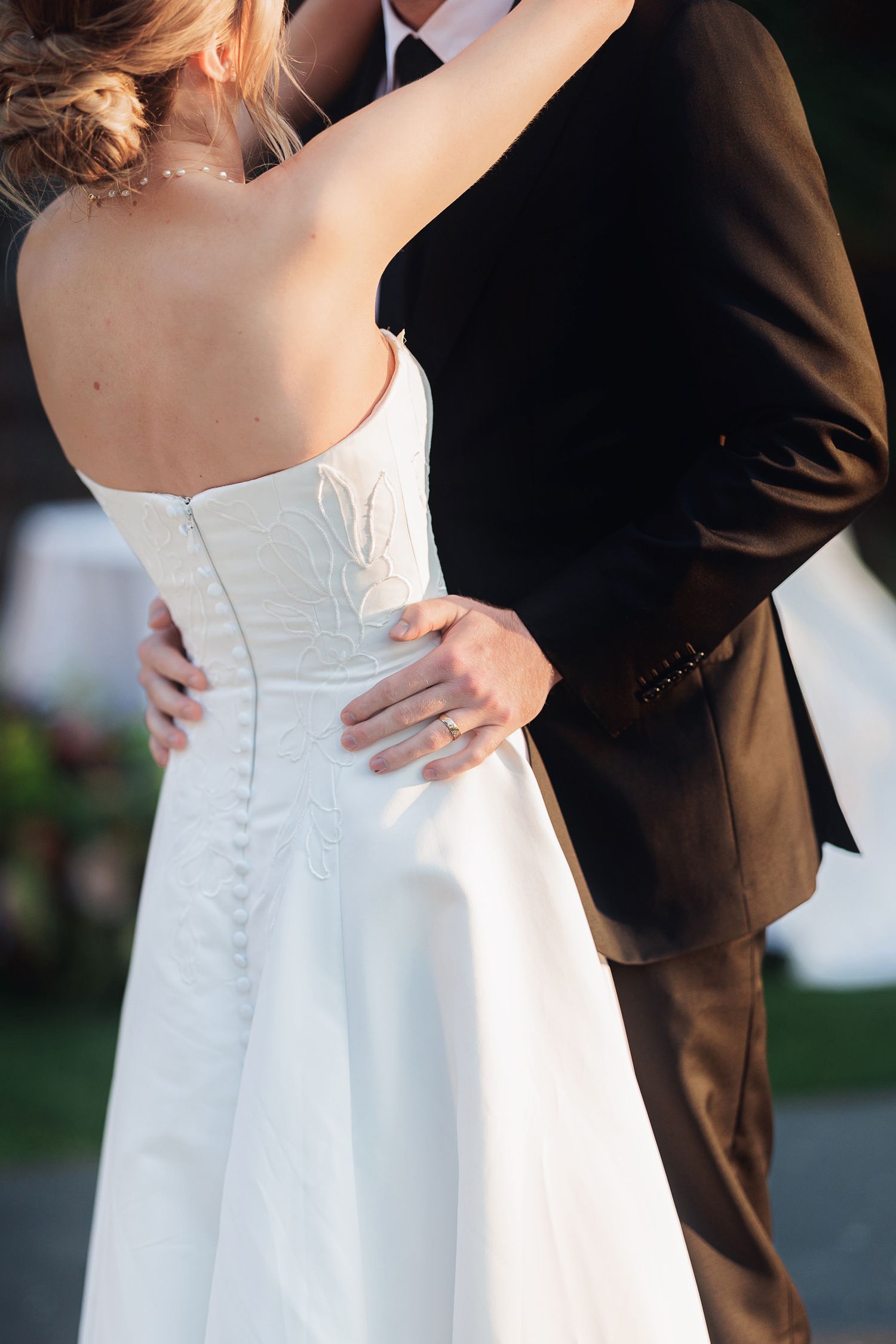 Bride and groom embracing during first dance, white strapless wedding gown with button back detail, groom in dark suit.