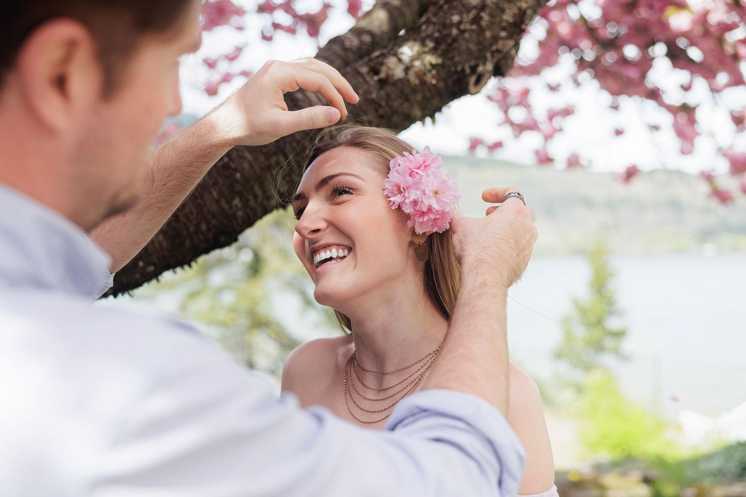 Man placing a pink flower in a smiling woman's hair under cherry blossom trees in spring.