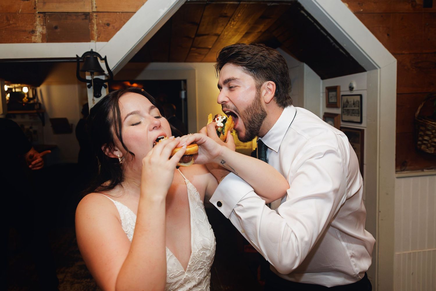 Bride and groom sharing a hot dog together at their wedding reception, laughing and enjoying a fun moment.