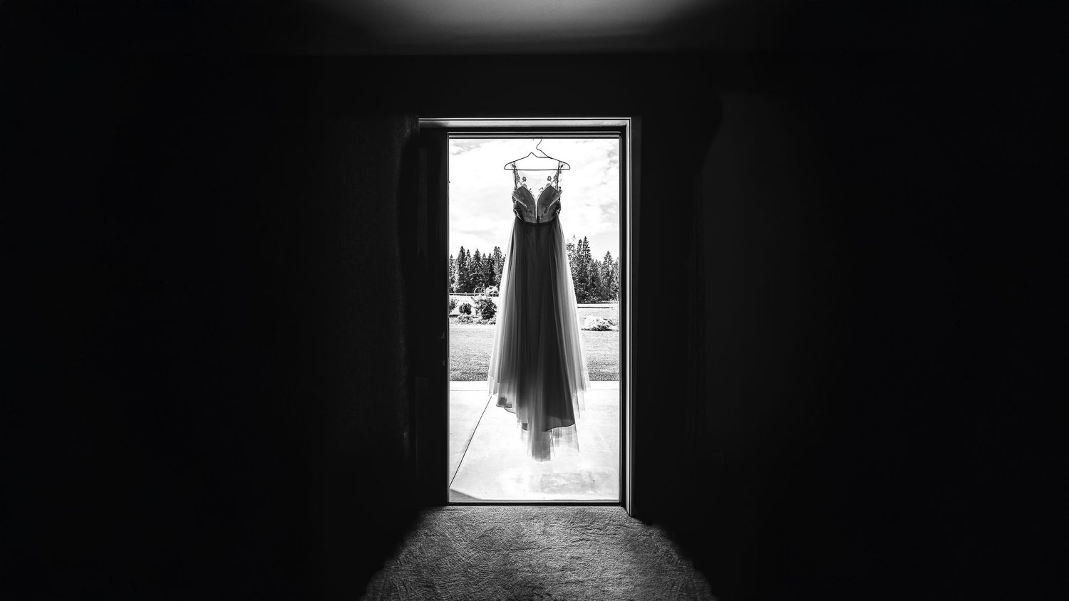 A wedding dress hangs ominously in a bright doorway, creating a striking silhouette against the light background.