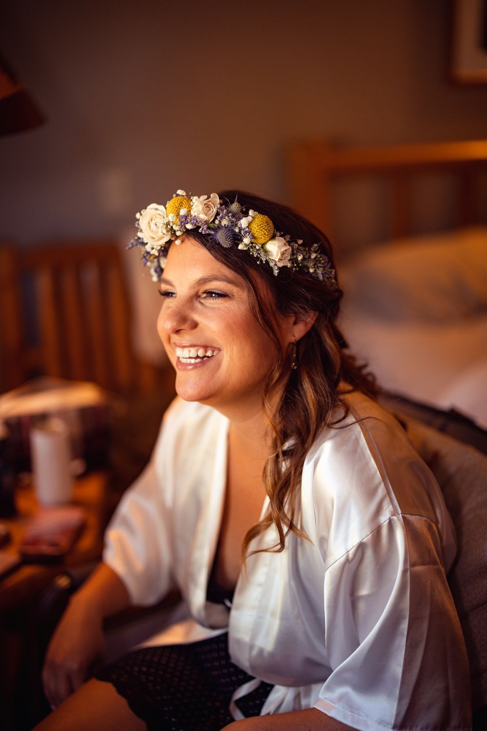 Someone wearing a white button-down shirt and floral crown laughs joyfully in warm indoor lighting.