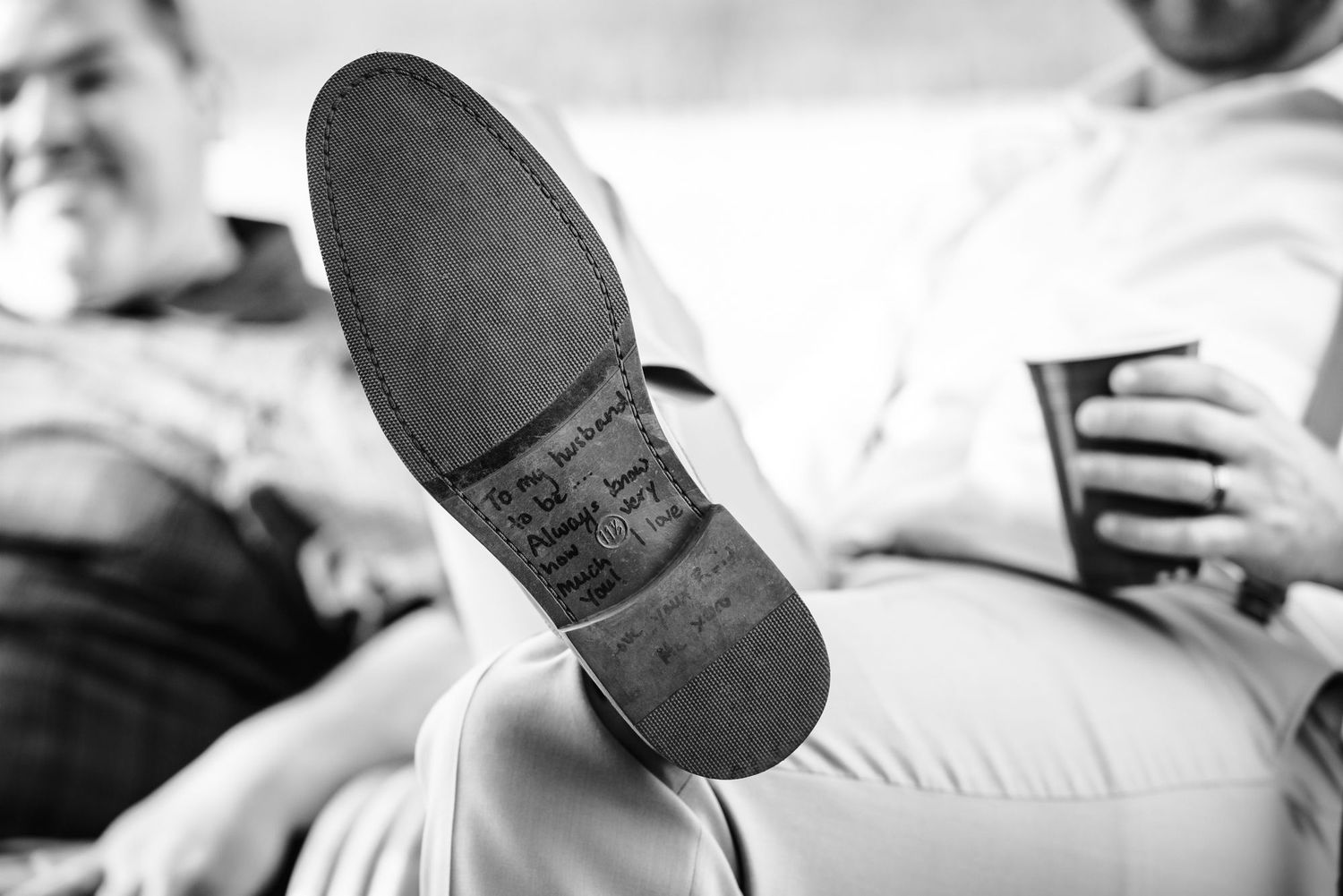 Black and white close-up of someone's shoe sole resting on a couch in a relaxed setting.