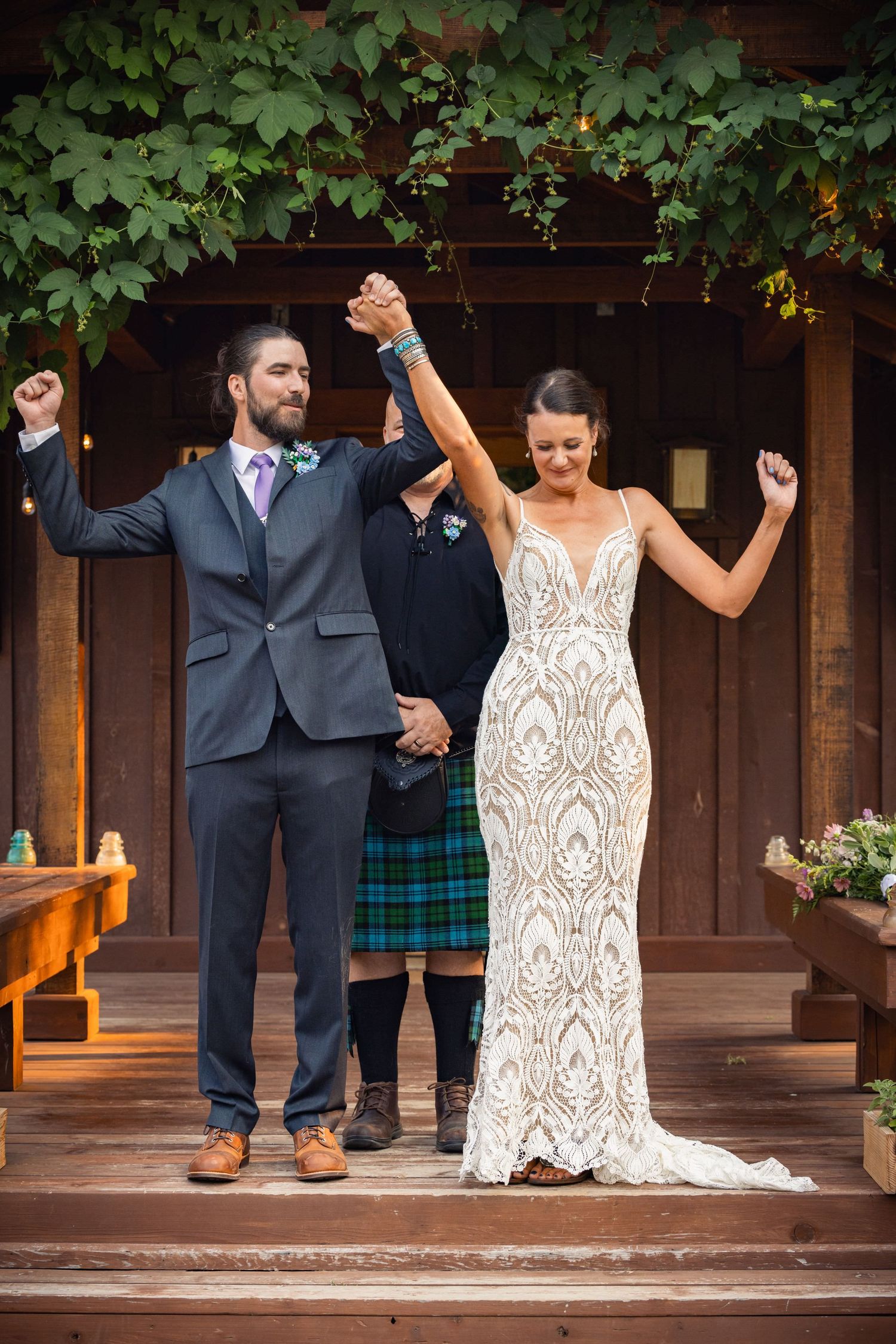 Jubilant newlyweds celebrate on wooden steps under green foliage at outdoor wedding ceremony.