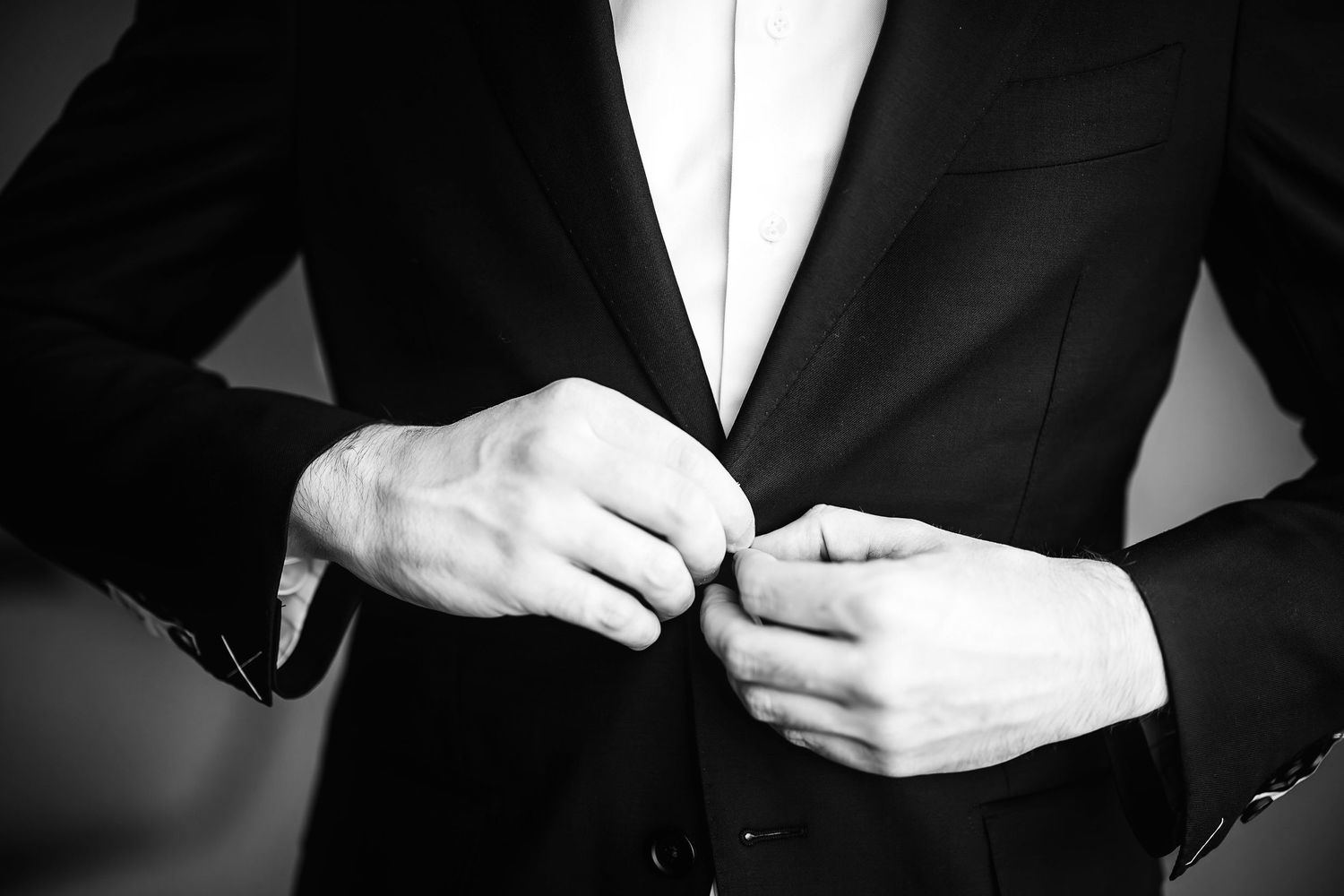 Black and white photo showing hands buttoning a formal black suit jacket.