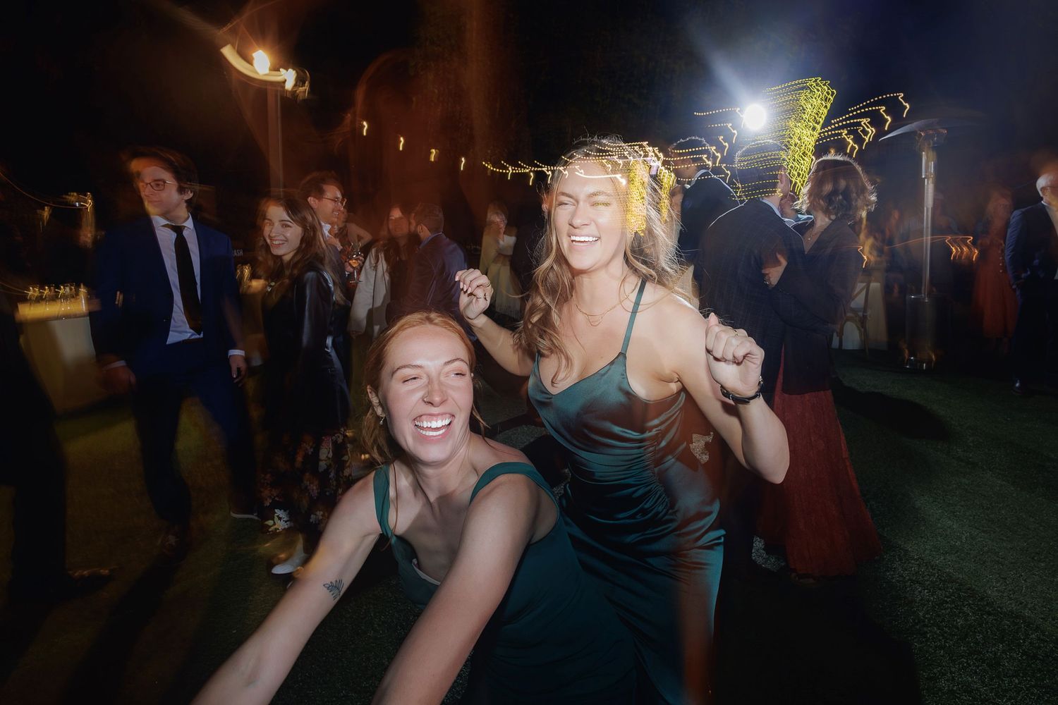 People dancing and celebrating at an outdoor nighttime party with string lights and festive atmosphere.