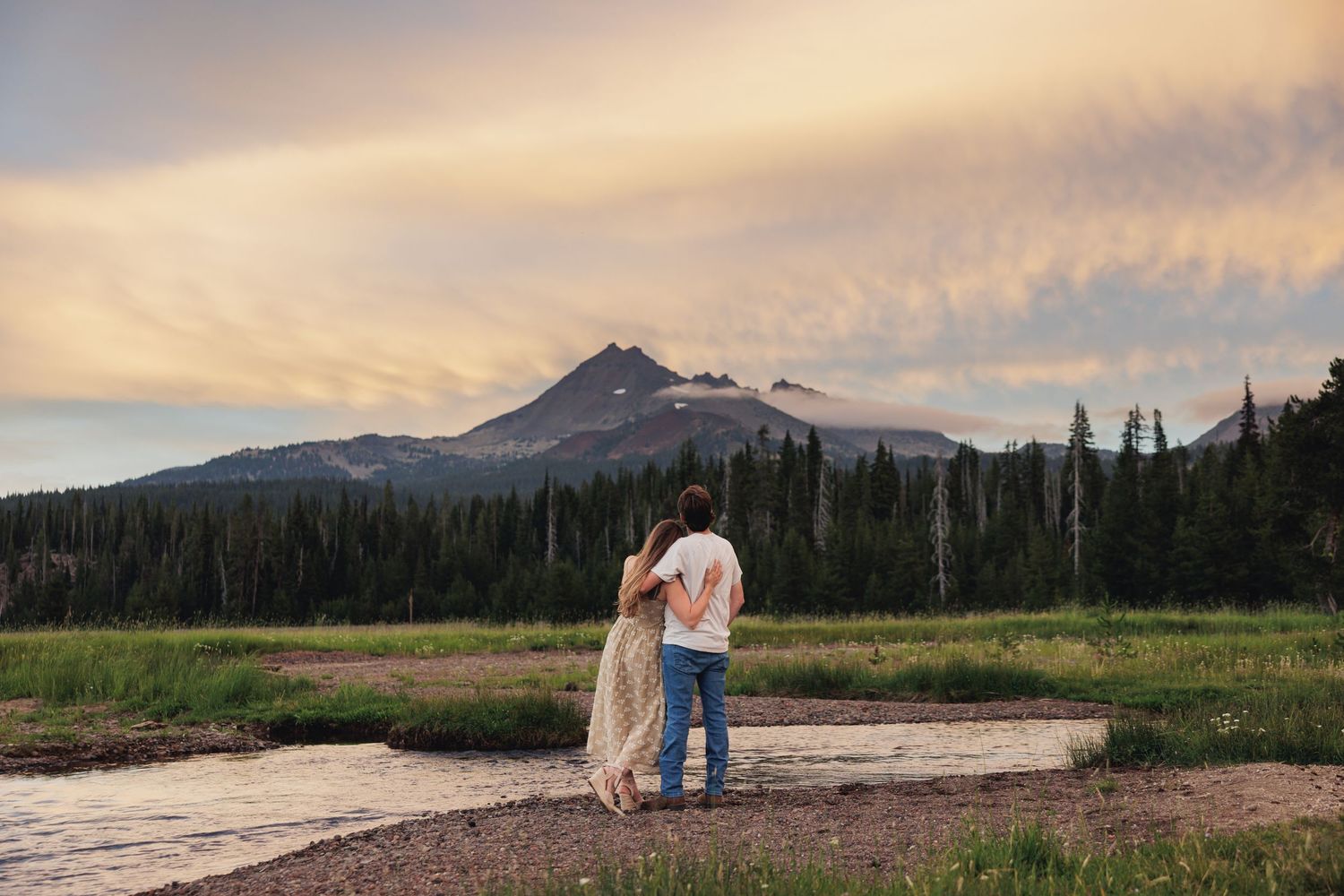 Romantic evening scene in mountain meadow with snow-capped peak and golden sunset sky in background.