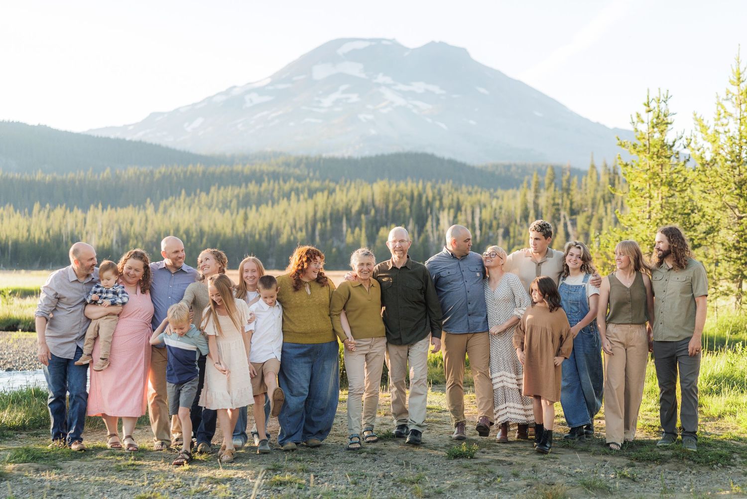 A group of people stand together posing for a photo in front of a scenic mountain and forest landscape at sunset.