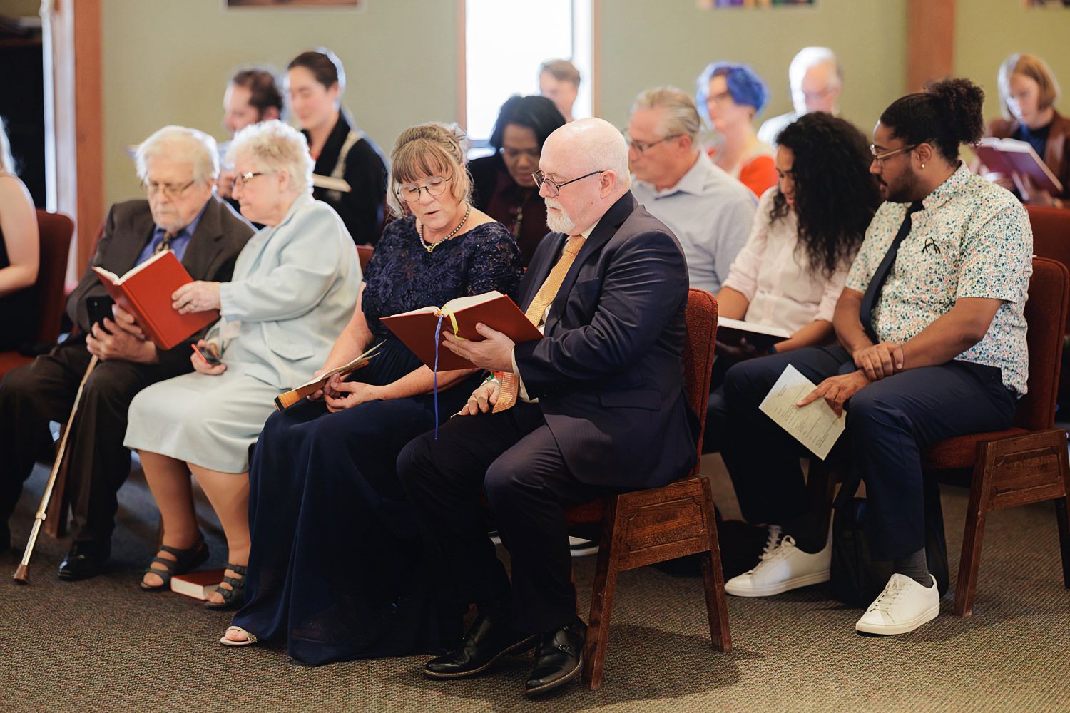People sit in a row of wooden pews during what appears to be a church service or gathering.