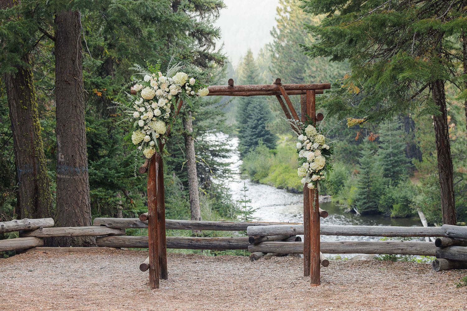 A serene forest path with wooden fence rails leads through tall evergreen trees on a sunny day.