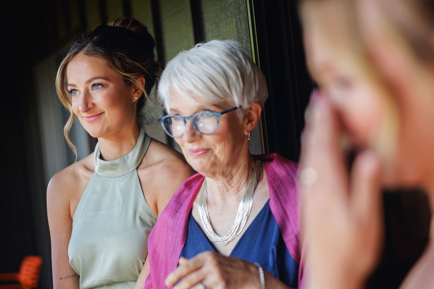 Young woman and elderly woman with blue glasses sharing a warm moment together at a wedding celebration.
