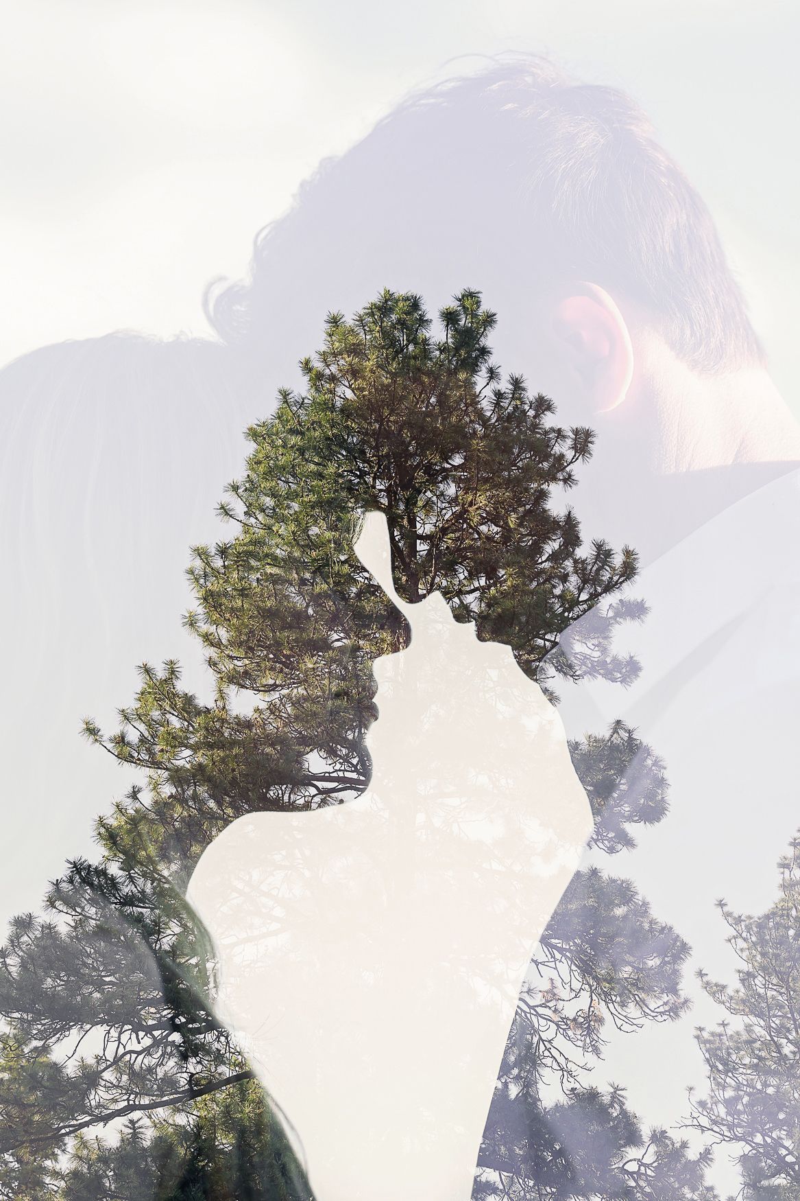 Double exposure portrait silhouette blends with pine trees against bright foggy sky near Bend, Oregon.