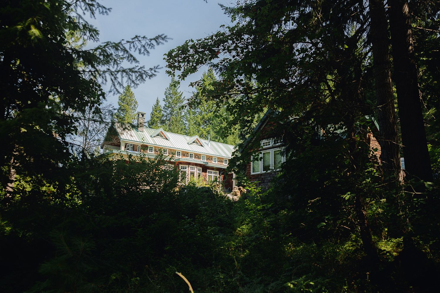 White house glimpsed through lush green forest trees on a sunny summer day.