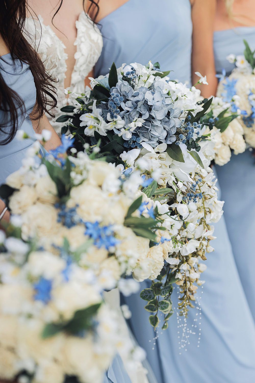 Beautiful wedding bouquets featuring blue hydrangeas, white flowers and cascading greenery against light blue bridesmaid dresses.