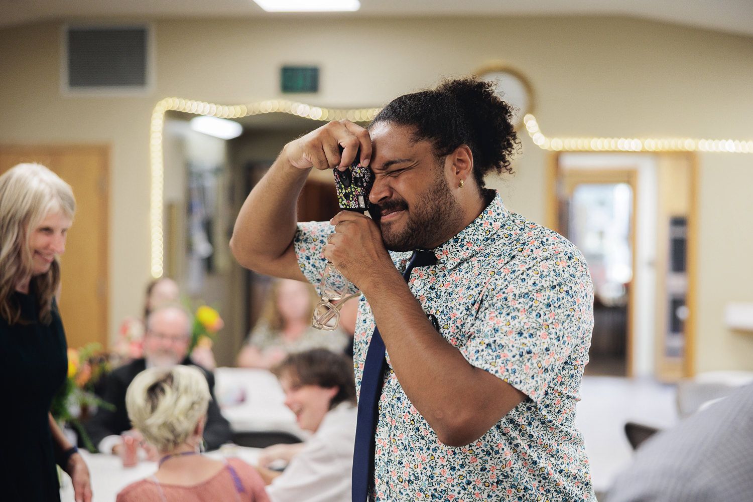 A person in a polka dot shirt laughs and gestures expressively during an animated conversation in an indoor setting.