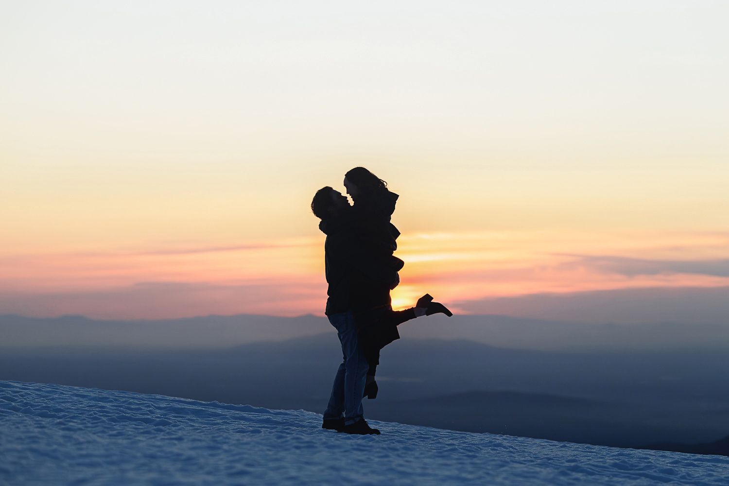 Silhouetted figure stands on a snowy mountainside against a dramatic sunset sky.