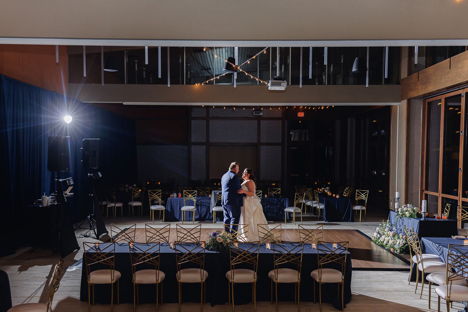Elegant wedding venue setup with dark wood floors and white decor elements illuminated by warm lighting.