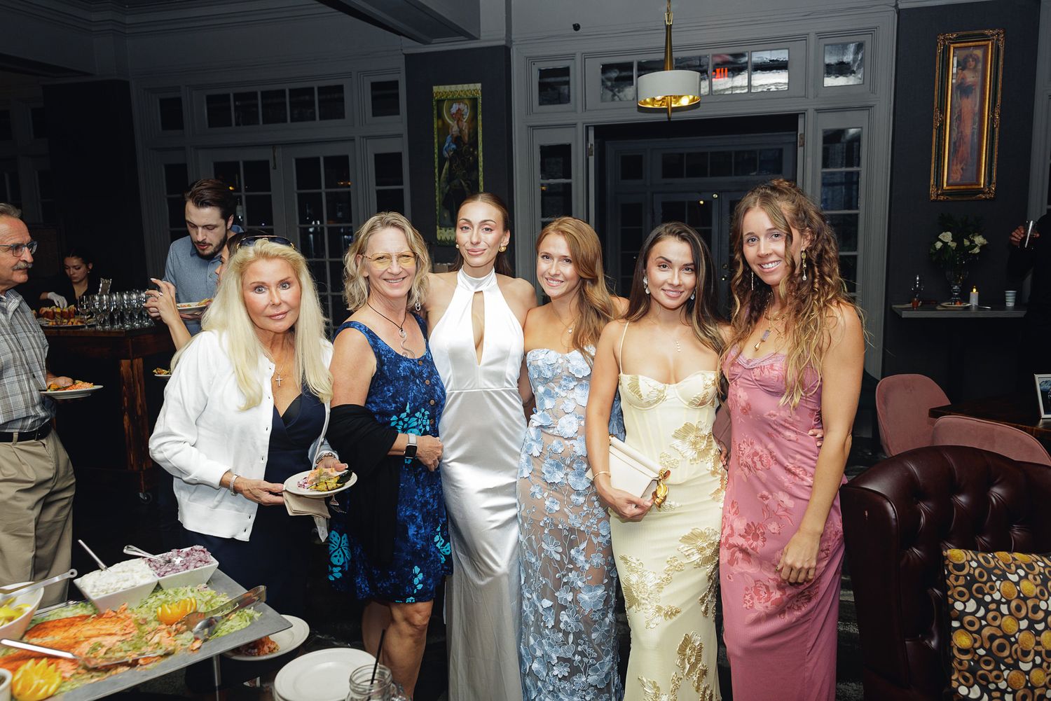 Group of elegantly dressed women posing together at a formal evening social event in a stylish venue.