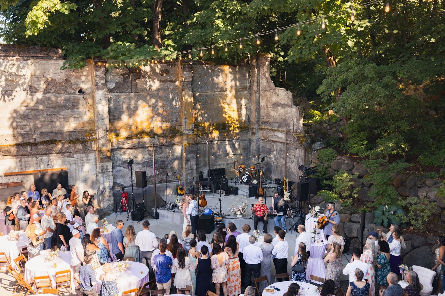Outdoor wedding reception at a rustic stone venue with string lights and guests mingling during golden hour.