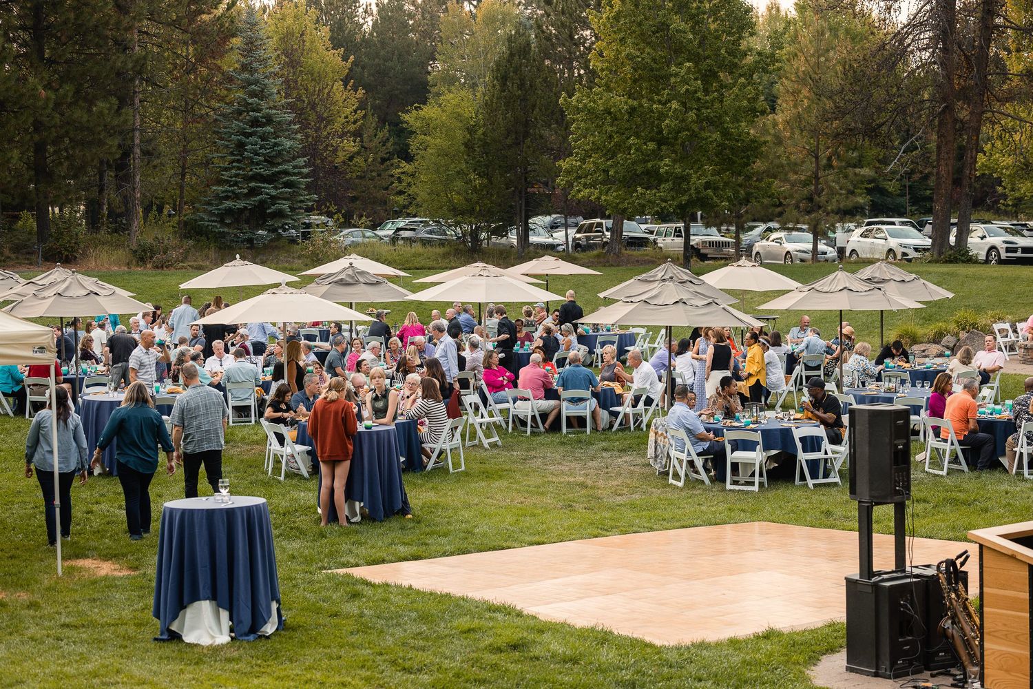 Outdoor wedding reception with white tents and tables set up on a grassy lawn surrounded by trees.