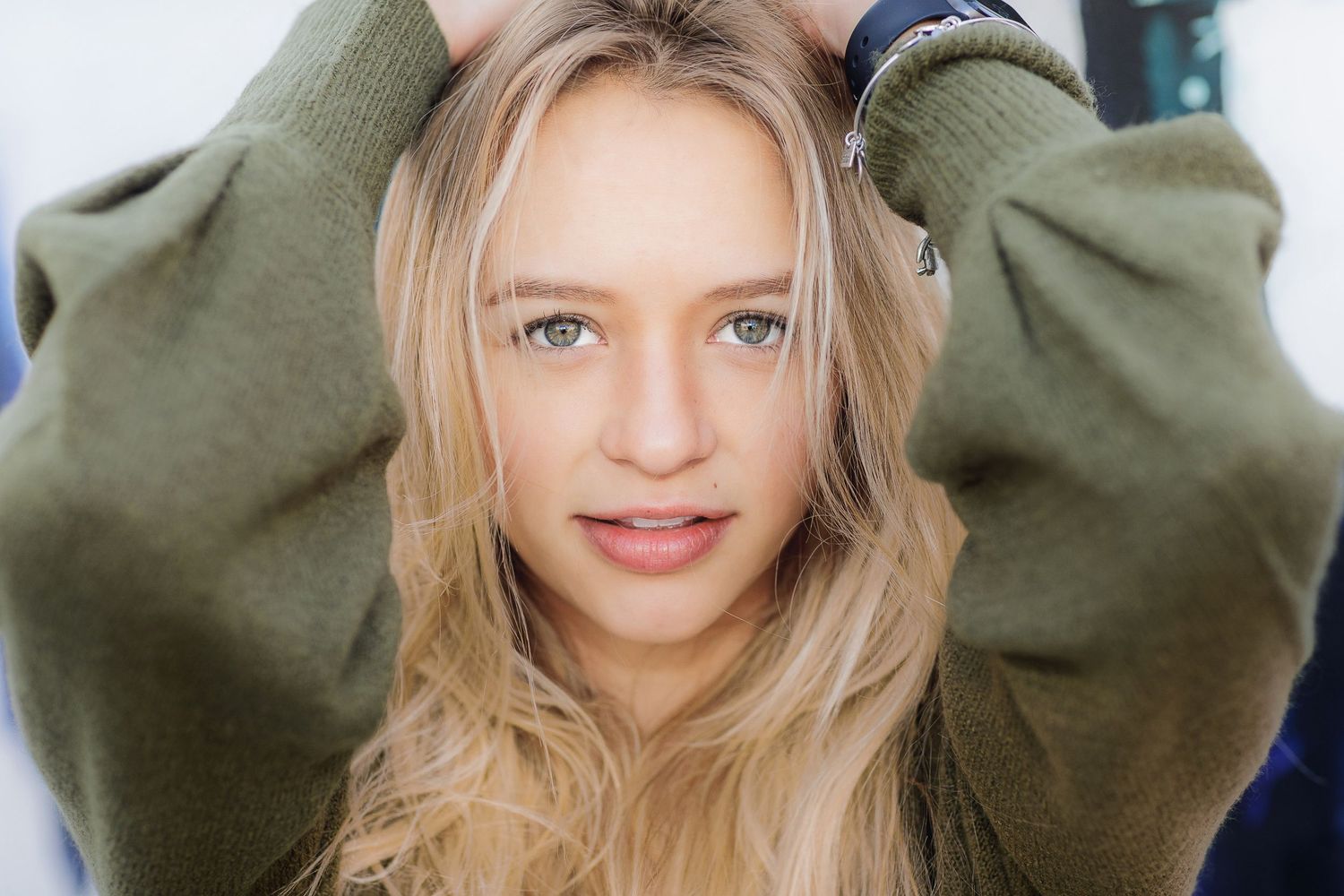 Portrait in oversized olive sweater against blurred background.