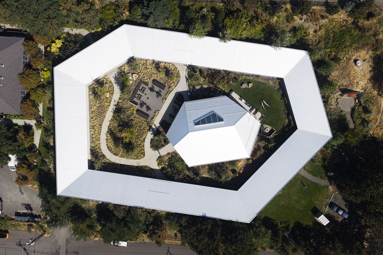 Aerial view of a unique white hexagonal building with an open courtyard and central glass structure surrounded by trees.