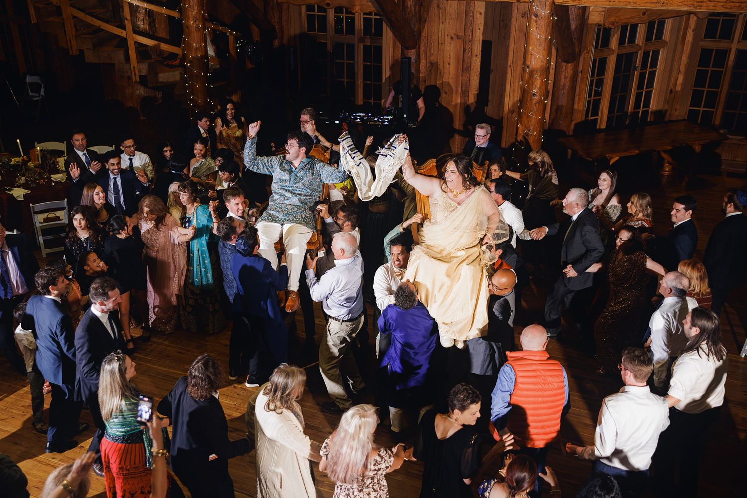 Wedding reception guests dancing joyfully in a rustic venue, with bride and groom celebrating on the dance floor.