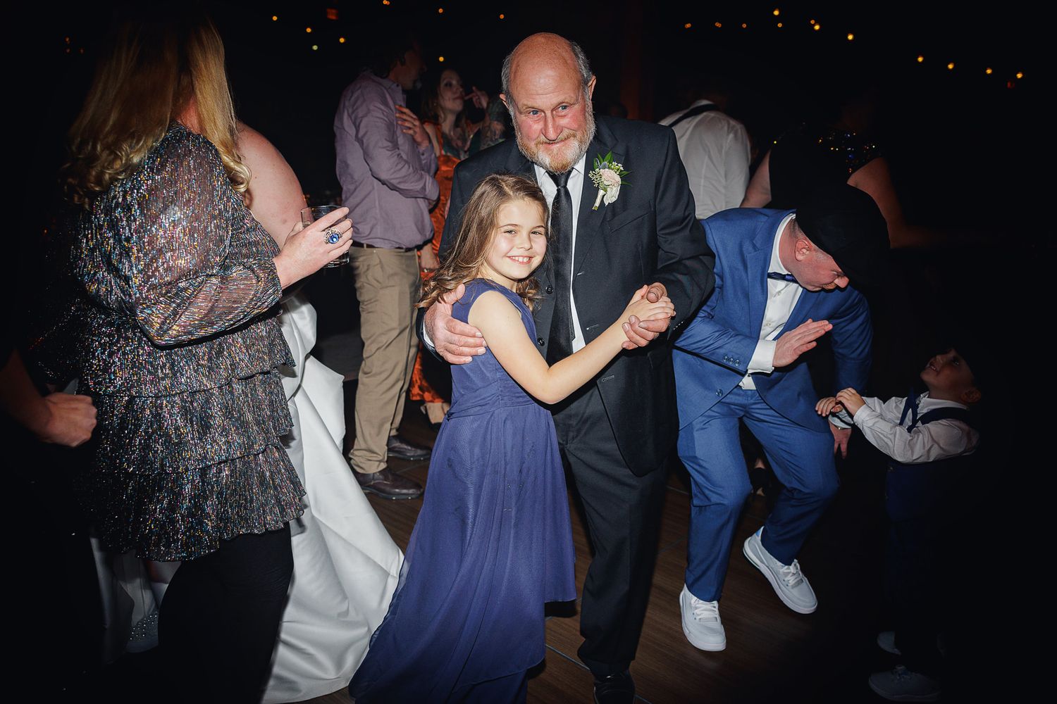People dancing together at a formal event with a young girl in a navy blue dress on the dance floor.