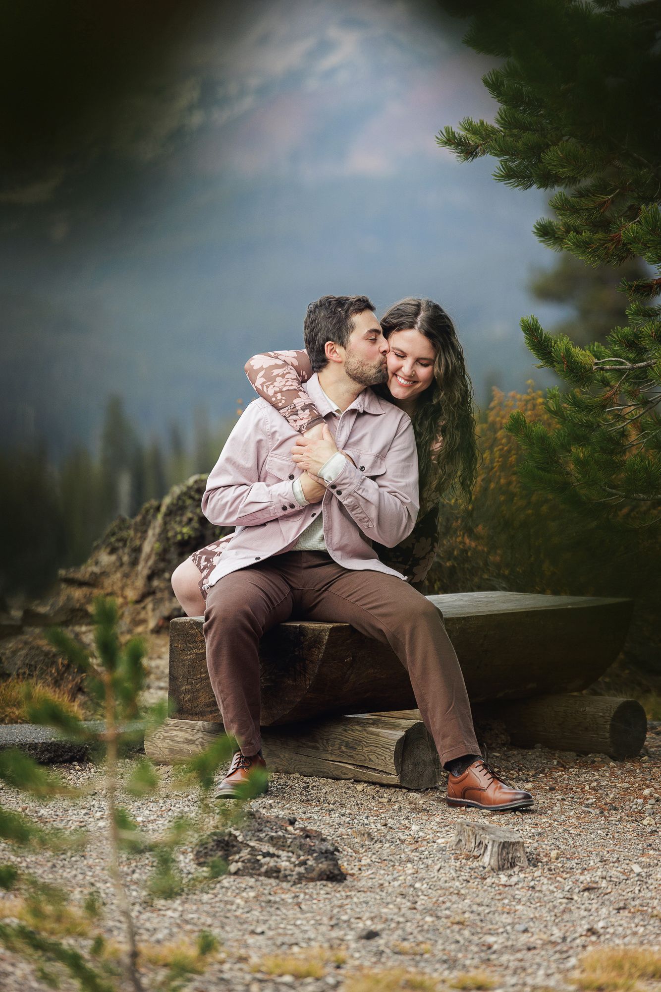 A couple shares an intimate moment while sitting on a rustic wooden bench surrounded by nature.
