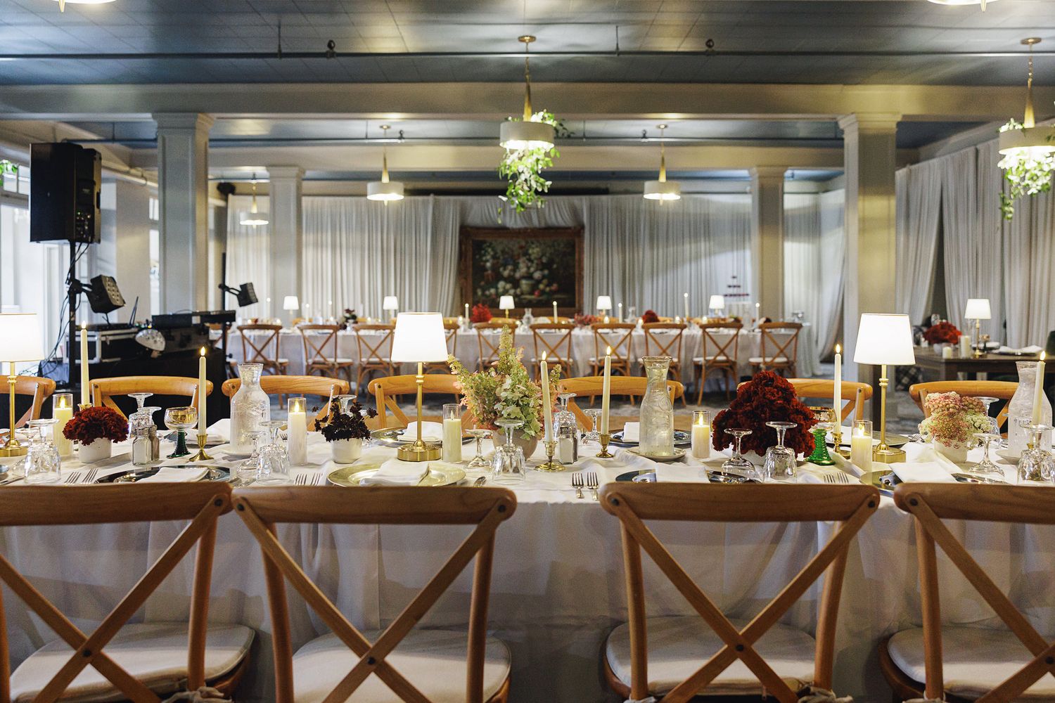Elegant banquet hall with long dining table, wooden cross-back chairs, white linens, and warm pendant lighting for an event.