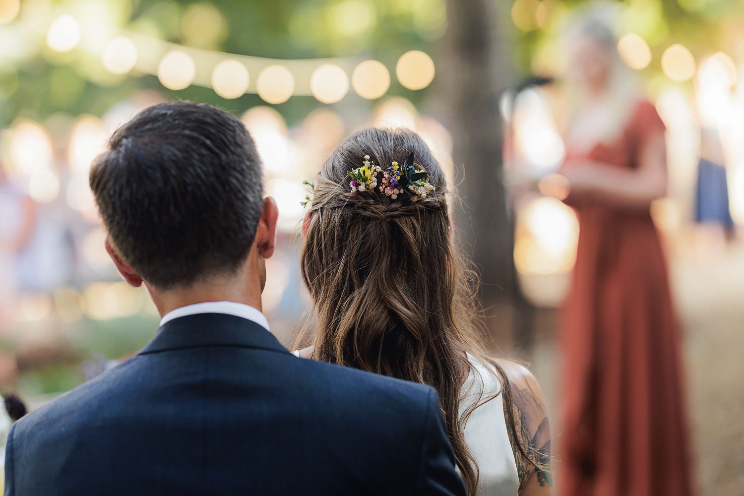 Wedding guests in formal attire at an outdoor reception with soft bokeh lights in the background.