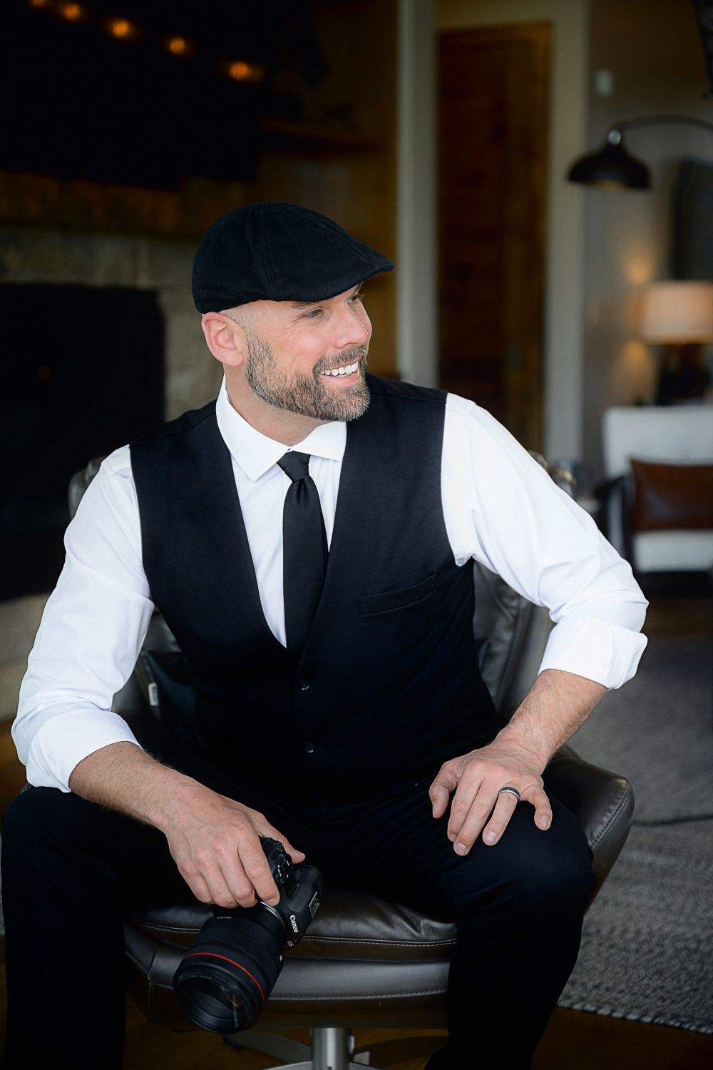 Professional wearing a black vest and white shirt smiles while working at a desk with a laptop.