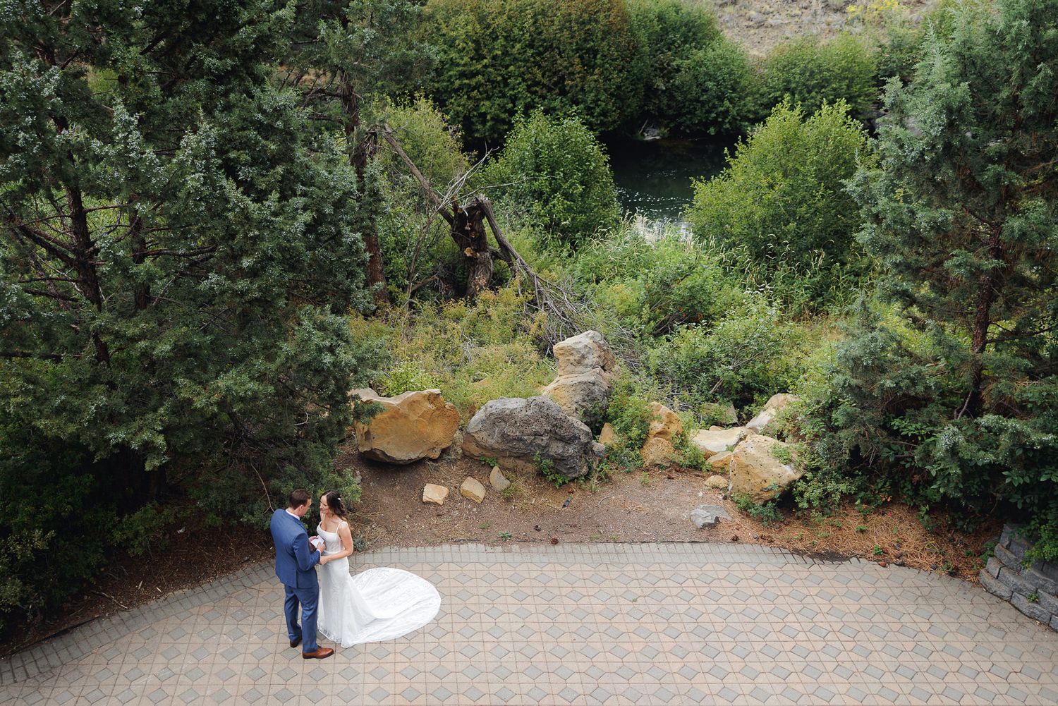 Wedding couple embraces in a lush garden setting with stone pathways and natural greenery.