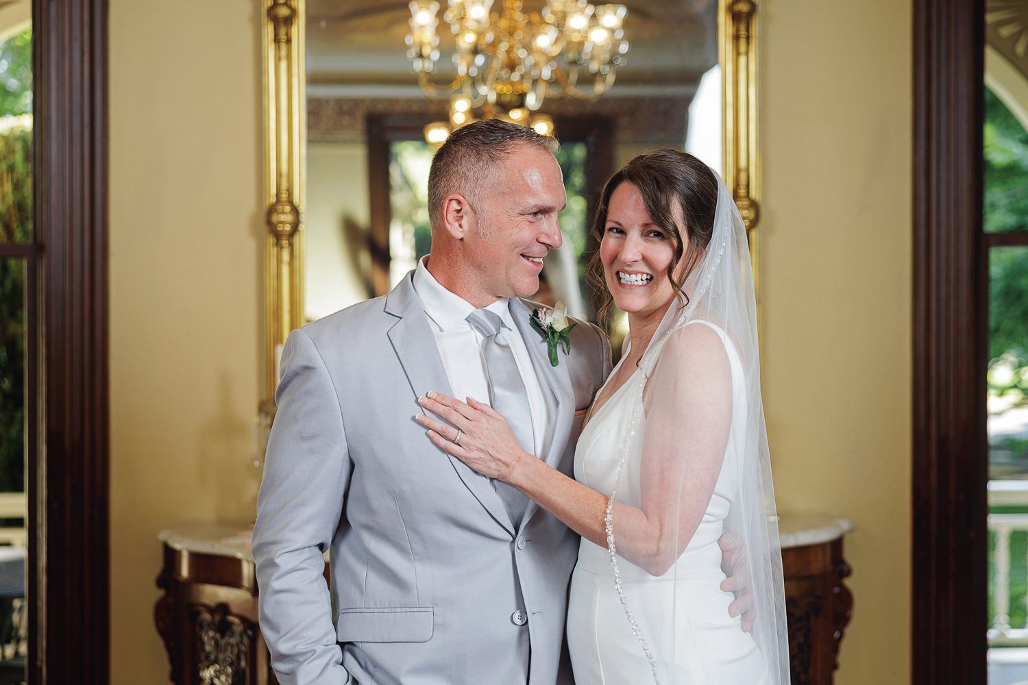 Two people share a joyful dance moment in an elegant room with chandeliers and ornate decor.