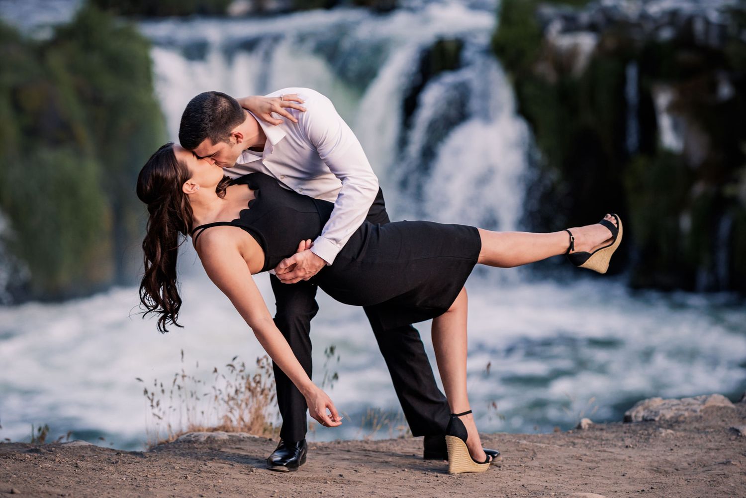 Romantic couple dances passionately near a scenic waterfall, with the person in black being dipped gracefully.