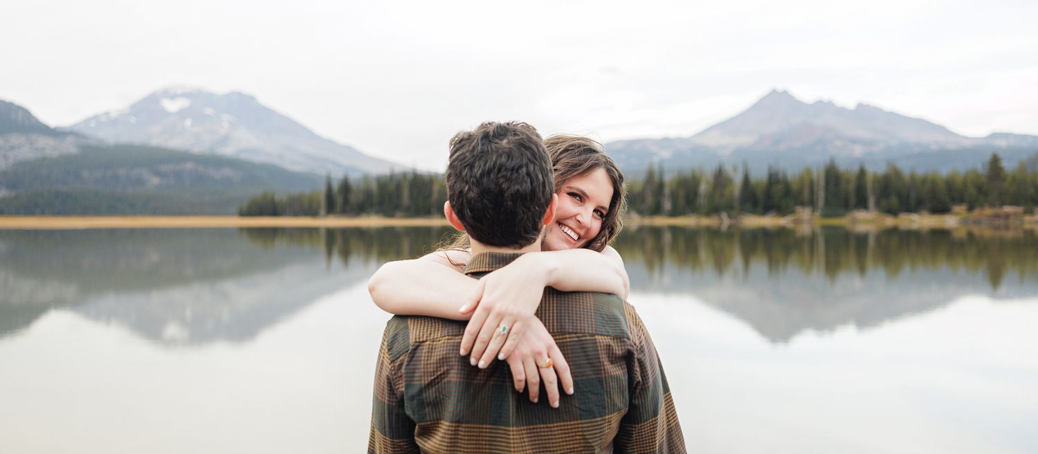 A couple embraces while enjoying scenic mountain and lake views in a romantic outdoor setting.