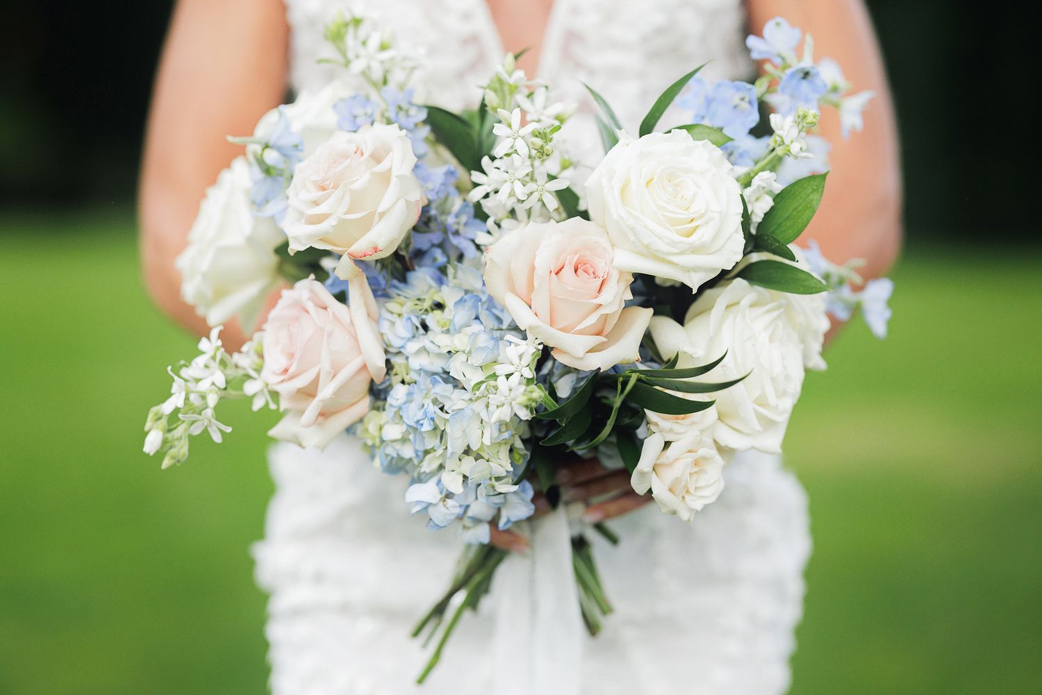 A beautiful bridal bouquet featuring white roses, pale blue hydrangeas, and delicate greenery against a blurred background.