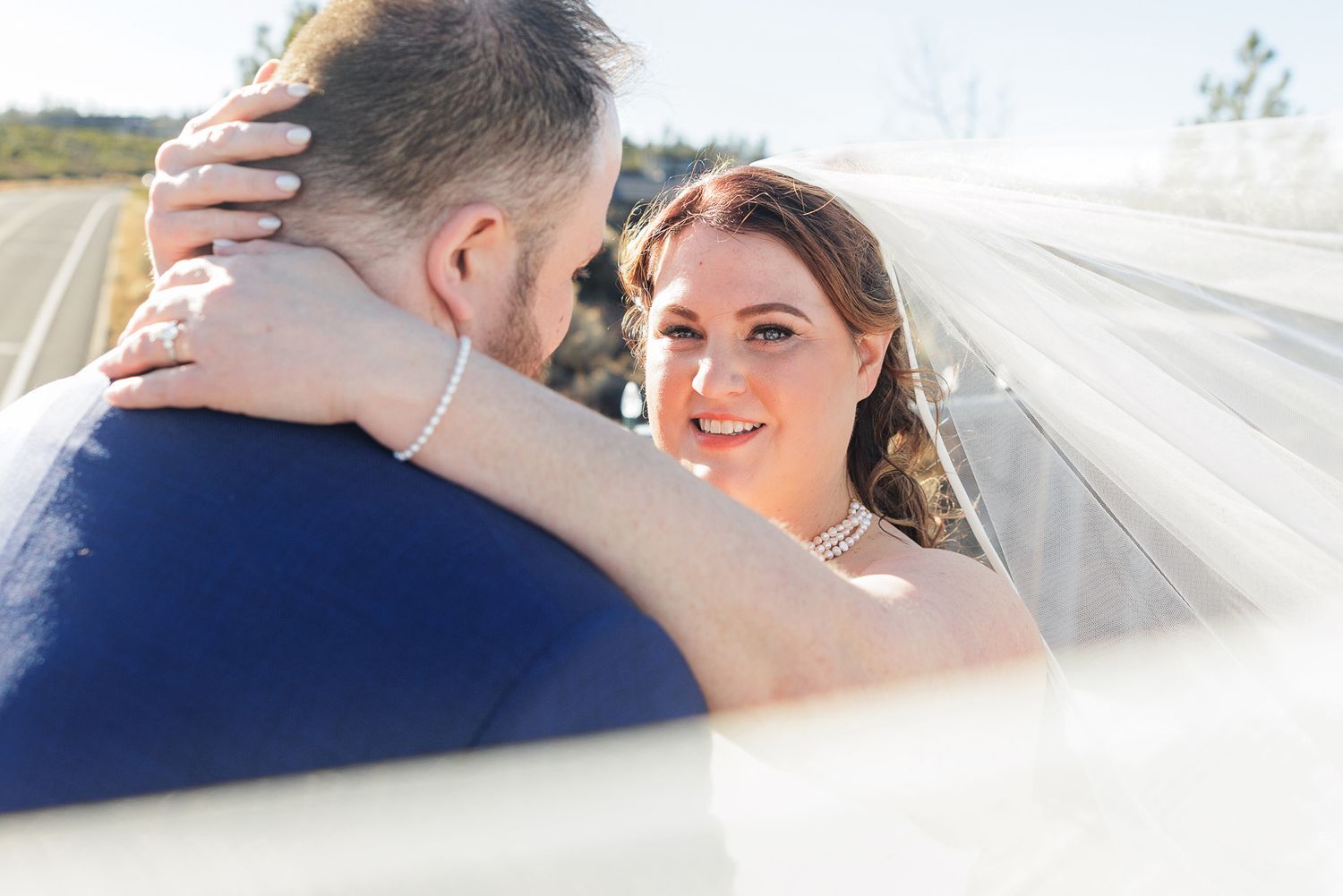 A romantic wedding couple shares intimate moments under a veil during their outdoor photo session.