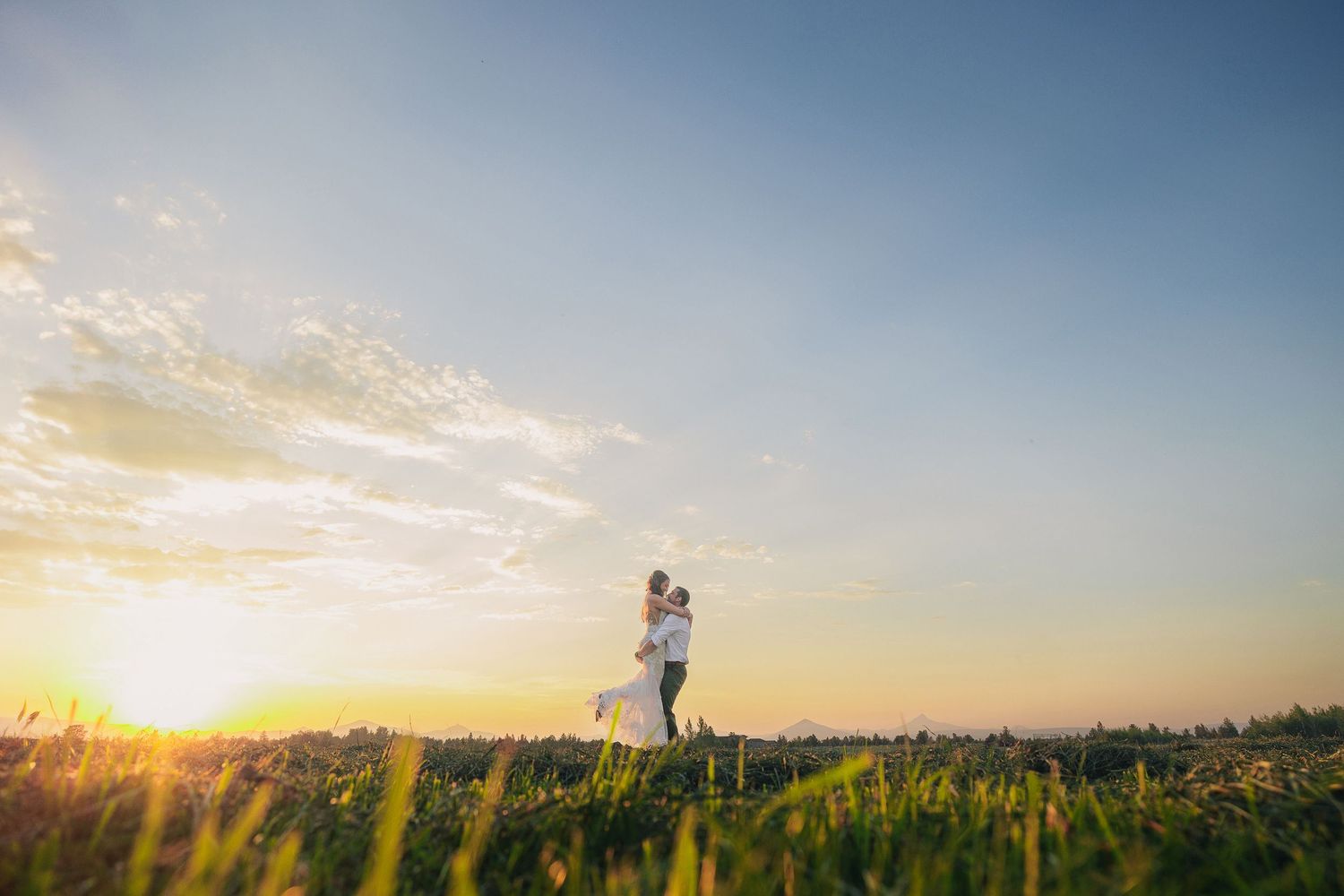 A silhouetted couple embraces in a field during golden hour sunset.