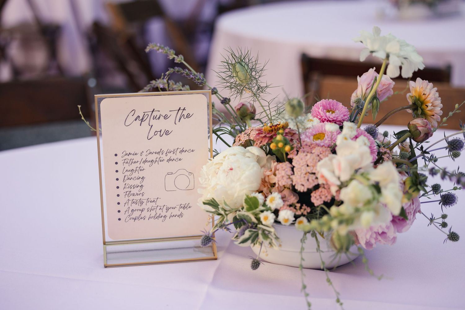 A wedding table setting with a floral centerpiece and cocktail menu card on a white tablecloth.