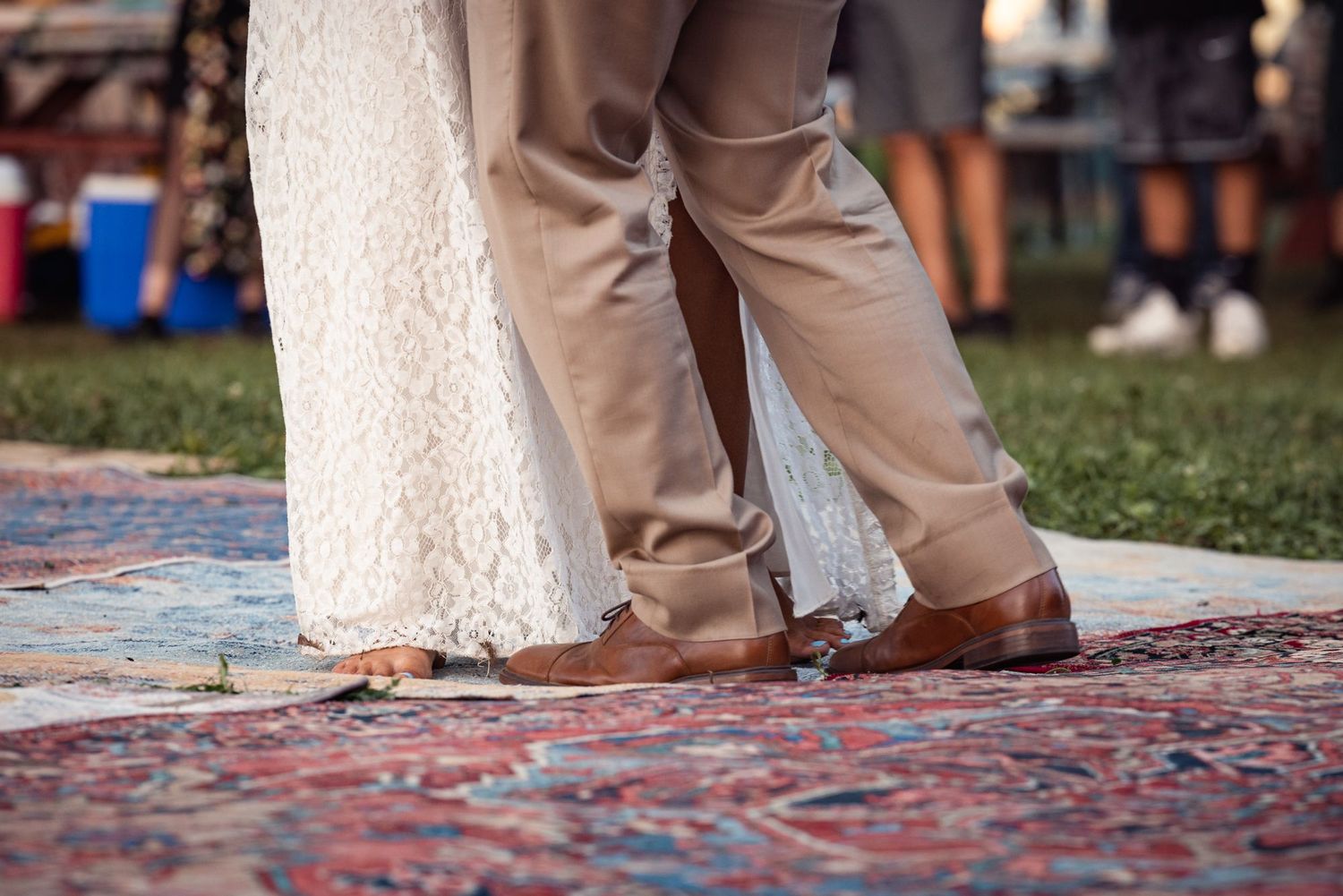 Close-up view of bride and groom's feet standing on a decorative oriental rug on grass at an outdoor wedding.