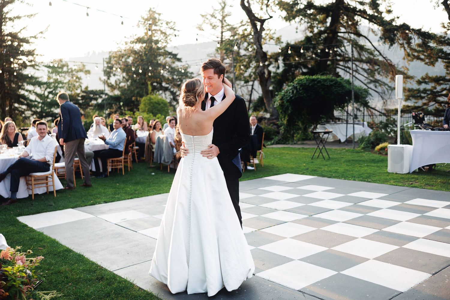 Bride and groom share first dance on checkered outdoor dance floor at elegant garden wedding reception.