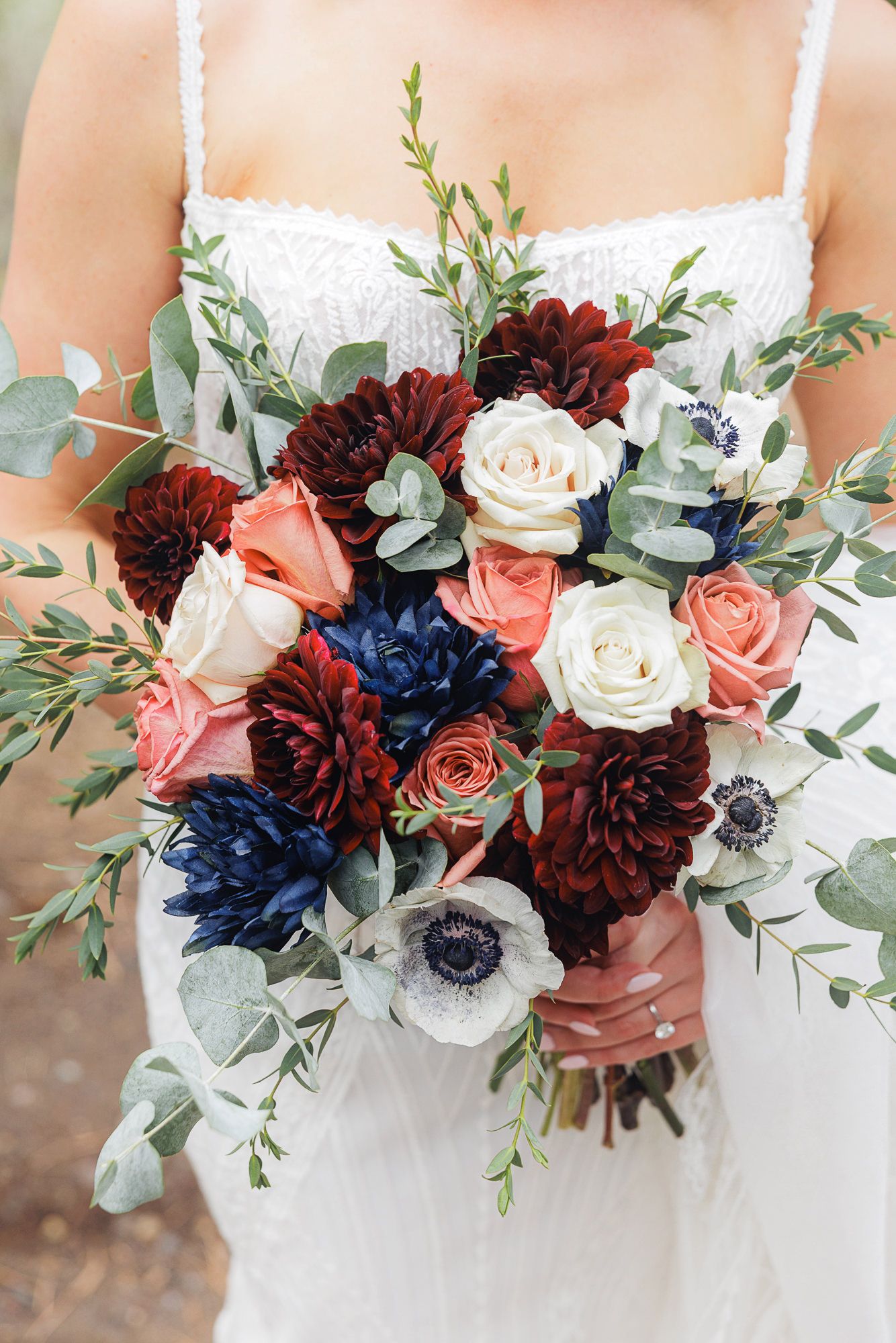 A bridal bouquet featuring burgundy dahlias, navy blue flowers, coral roses, white roses and eucalyptus greenery.