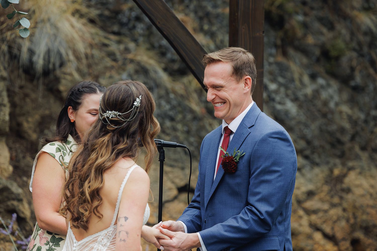A couple shares an emotional moment during their outdoor wedding ceremony against a rocky backdrop.