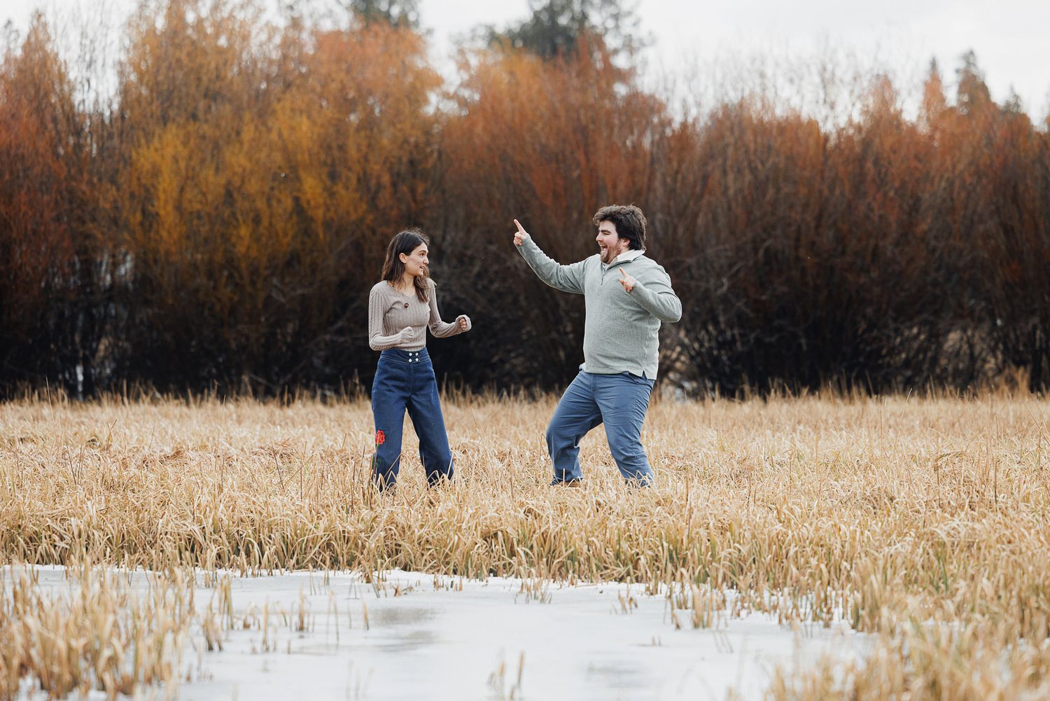 Two people playfully run through a golden autumn field during sunset.
