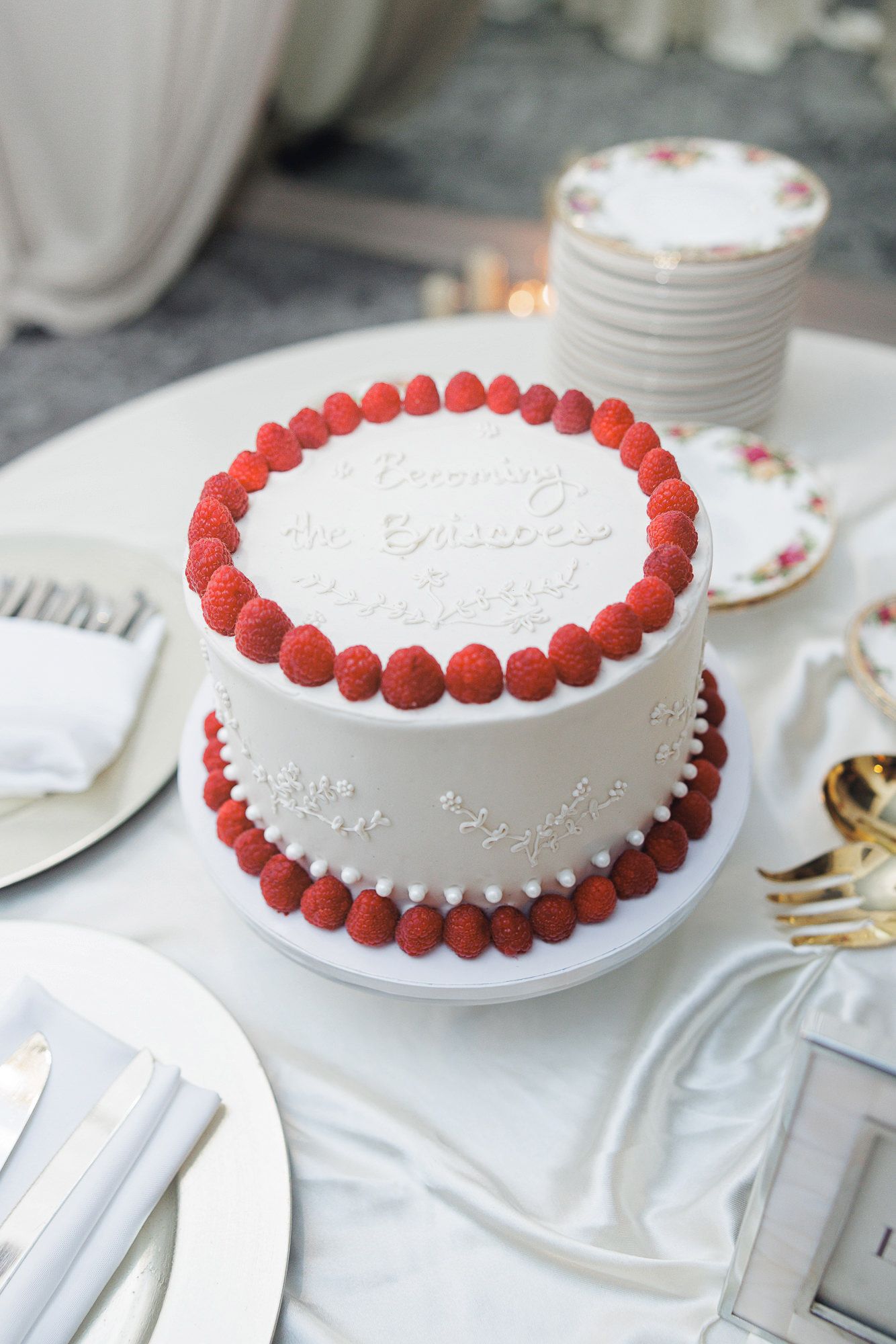Elegant two-tier white wedding cake decorated with fresh raspberries and script lettering on display.