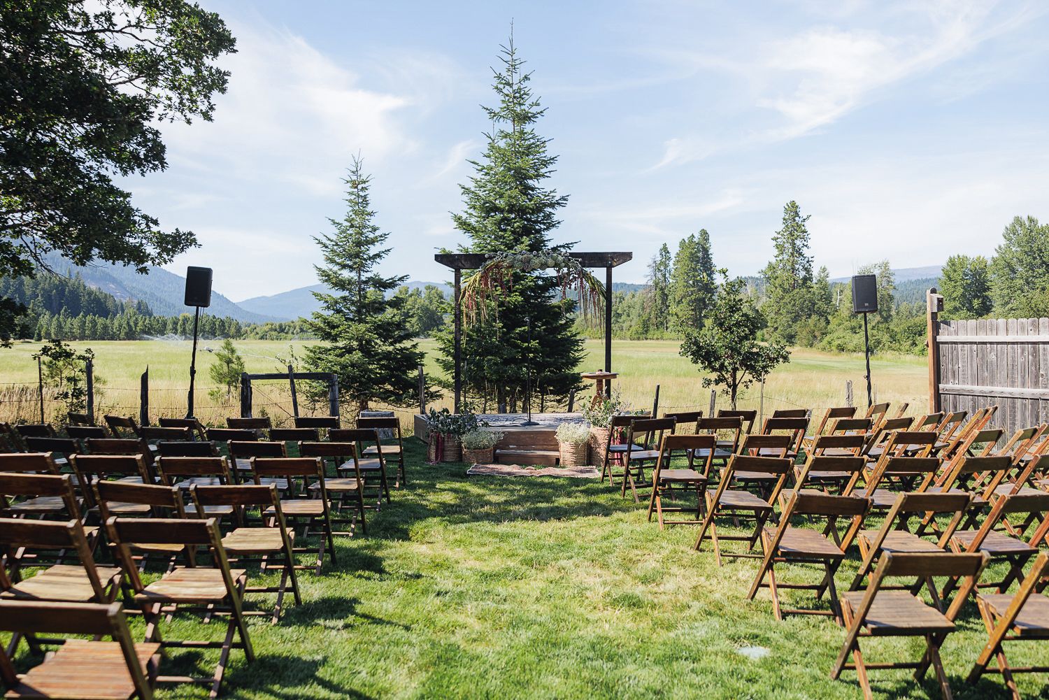 Wooden chairs arranged for an outdoor wedding ceremony with evergreen trees and mountains in the background.